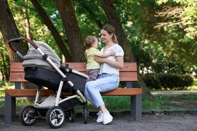 Happy nanny with cute little boy on bench in park