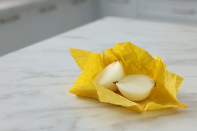 Halves of onion with yellow beeswax food wrap on white marble table, space for text