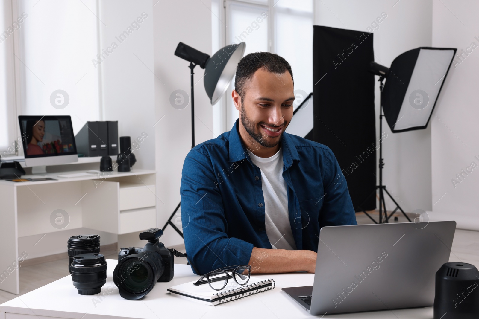 Photo of Young professional photographer with camera working on laptop in modern photo studio