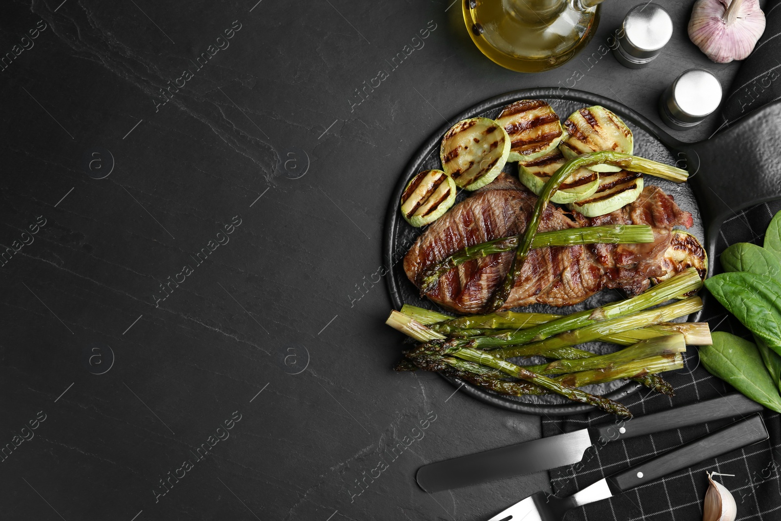 Photo of Tasty grilled meat served with asparagus and zucchini on black table, flat lay. Space for text