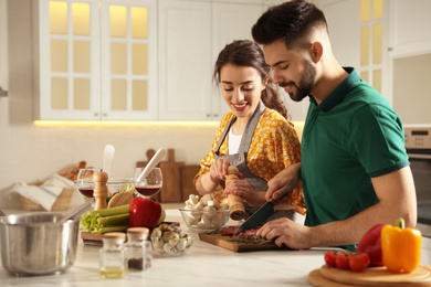 Photo of Lovely young couple cooking meat together in kitchen