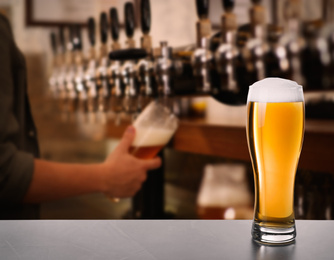 Fresh cold beer on table and bartender in pub, space for text