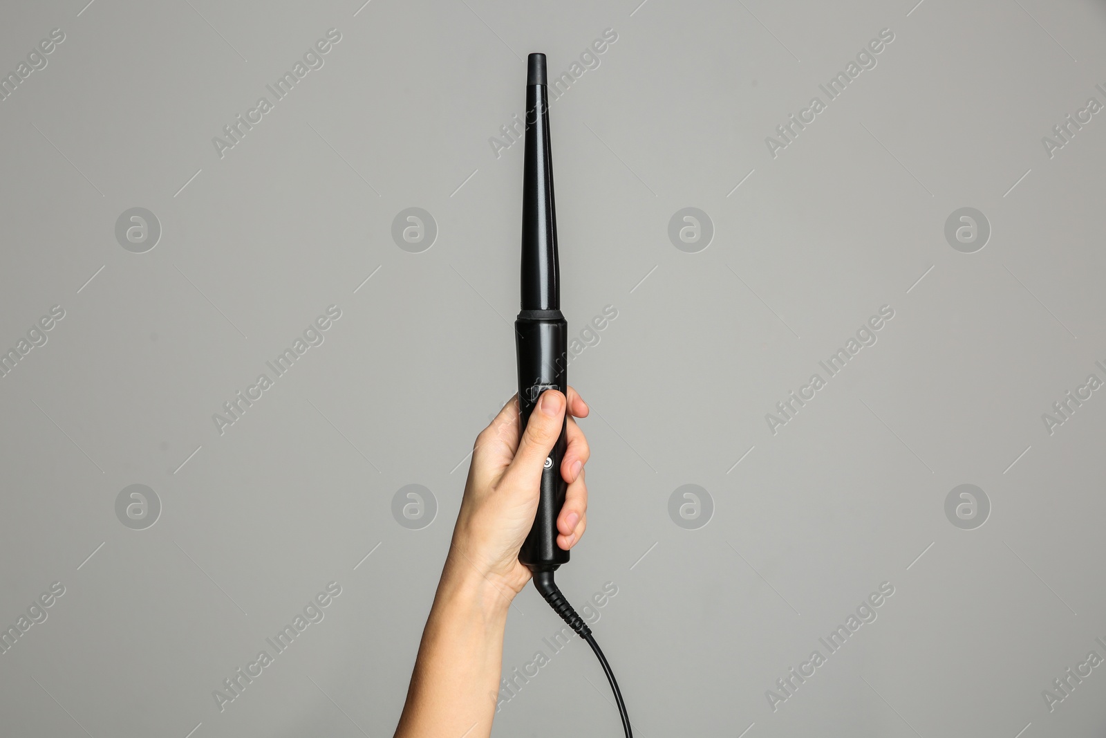 Photo of Woman holding clipless curling hair iron on light grey background, closeup