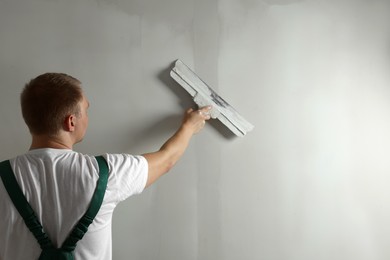 Photo of Professional worker plastering wall with putty knife. Space for text