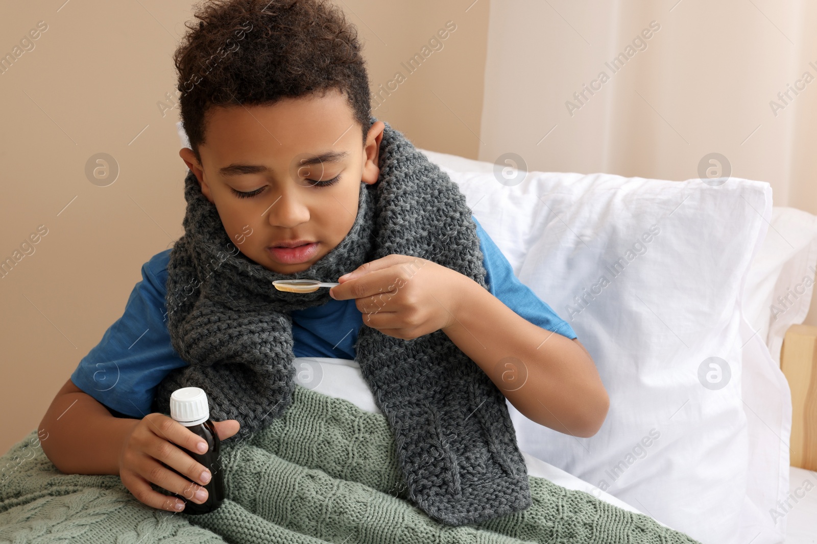 Photo of African-American boy taking cough syrup on bed at home. Cold medicine