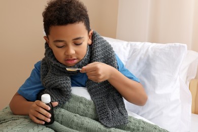 Photo of African-American boy taking cough syrup on bed at home. Cold medicine