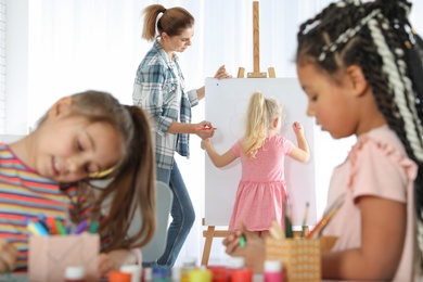 Female teacher with child near easel at painting lesson indoors