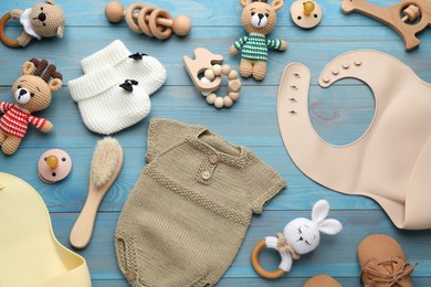 Photo of Flat lay composition with silicone baby bibs, clothes and accessories on light blue wooden background