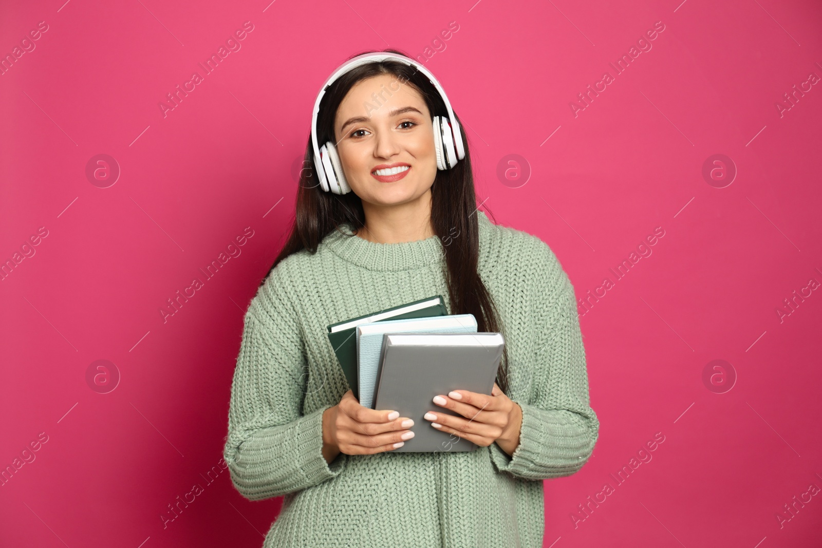 Photo of Young woman listening to audiobook on pink background