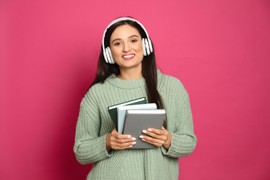 Young woman listening to audiobook on pink background