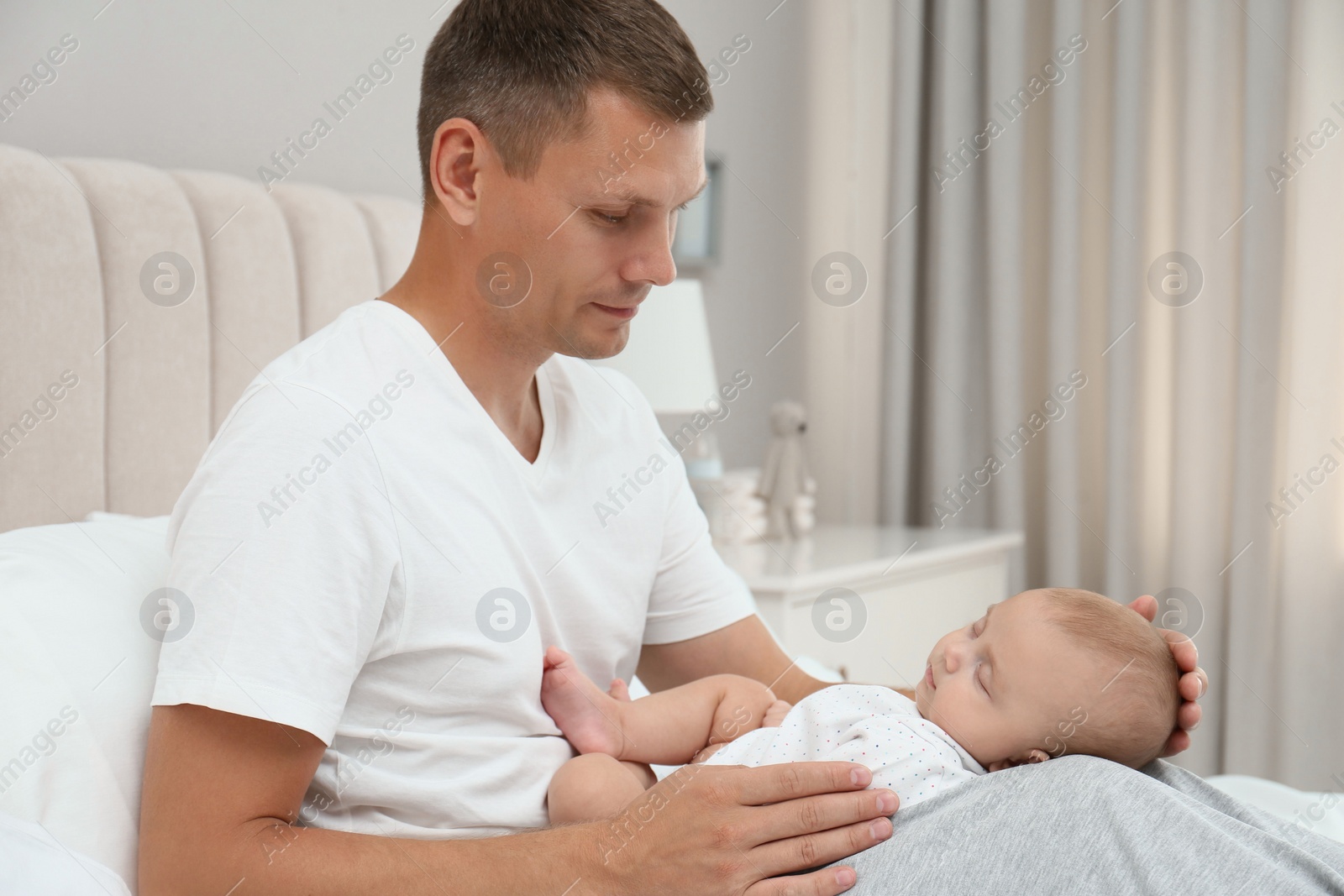 Photo of Happy father holding his cute sleeping baby on bed at home