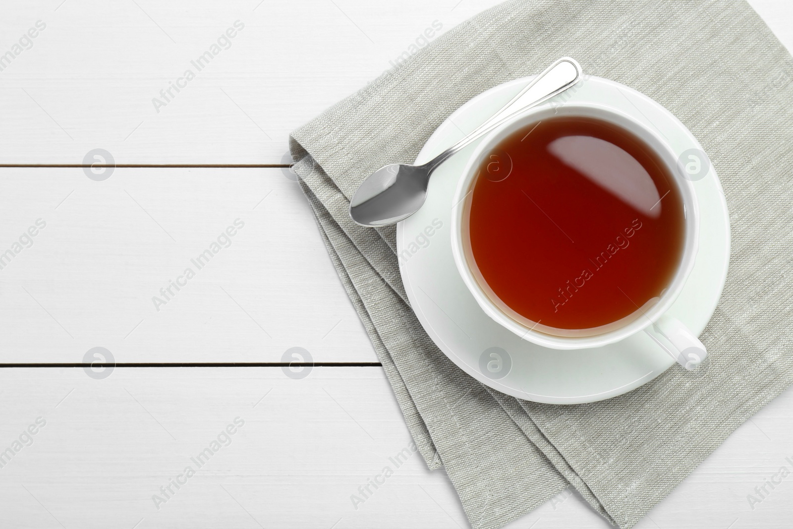 Photo of Aromatic tea in cup and spoon on white wooden table, top view. Space for text