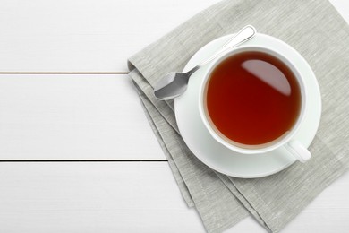 Photo of Aromatic tea in cup and spoon on white wooden table, top view. Space for text