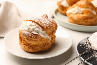 Photo of Delicious profiteroles with cream filling and powdered sugar on white table, closeup