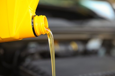 Photo of Pouring motor oil from yellow container against blurred background, closeup. Space for text