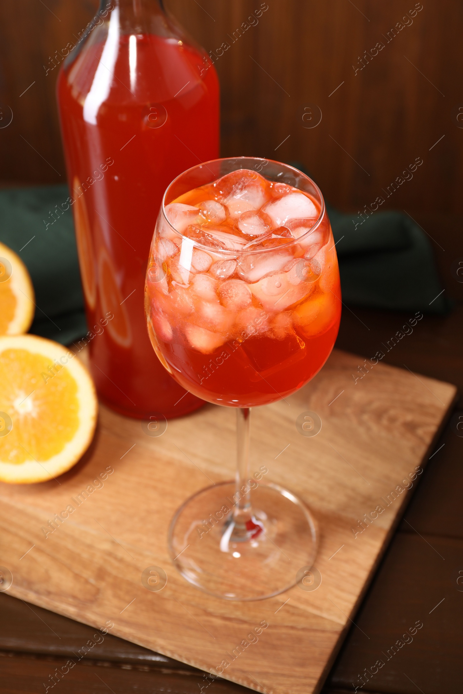 Photo of Aperol spritz cocktail and ice cubes in glass and bottle on wooden table, closeup