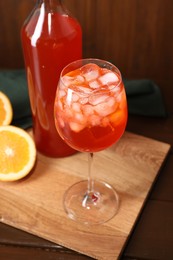 Photo of Aperol spritz cocktail and ice cubes in glass and bottle on wooden table, closeup