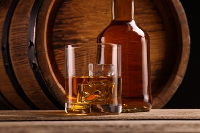 Photo of Whiskey with ice cubes in glass, bottle and barrel on wooden table