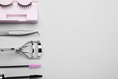 Flat lay composition with fake eyelashes, brushes and tools on light grey background. Space for text