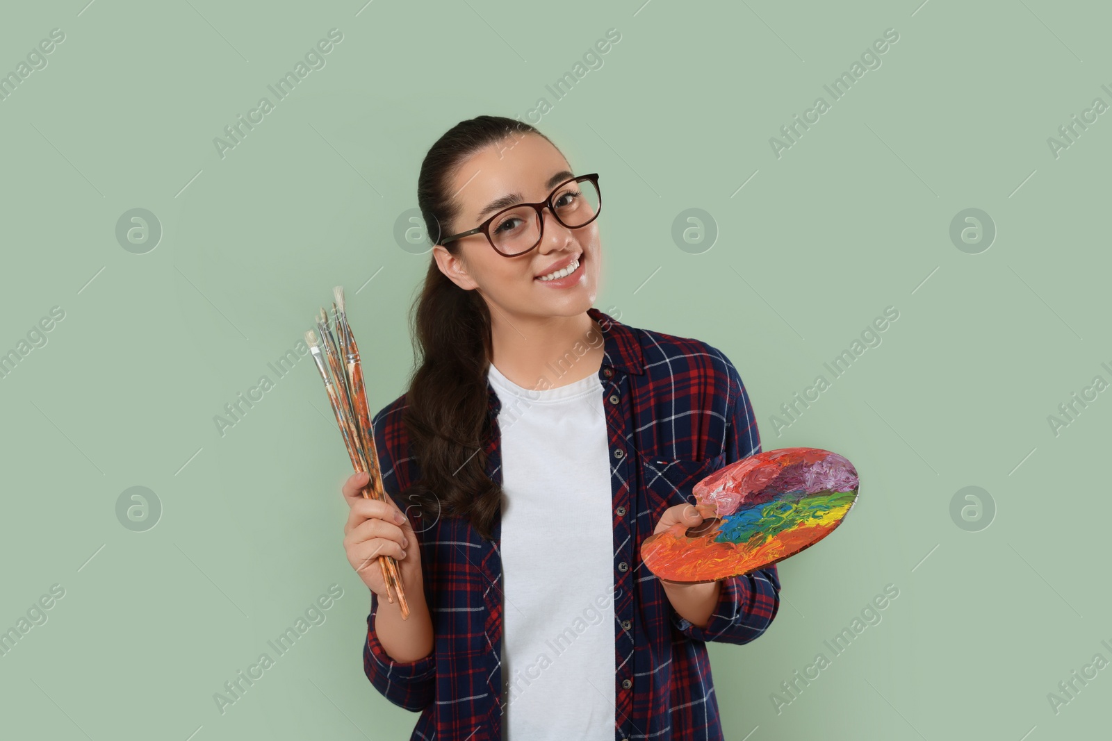 Photo of Woman with painting tools on pale green background. Young artist