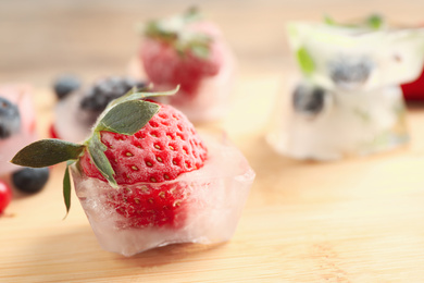 Photo of Ice cube with frozen strawberry on wooden table, closeup. Space for text