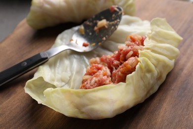 Photo of Preparing stuffed cabbage roll on wooden board, closeup