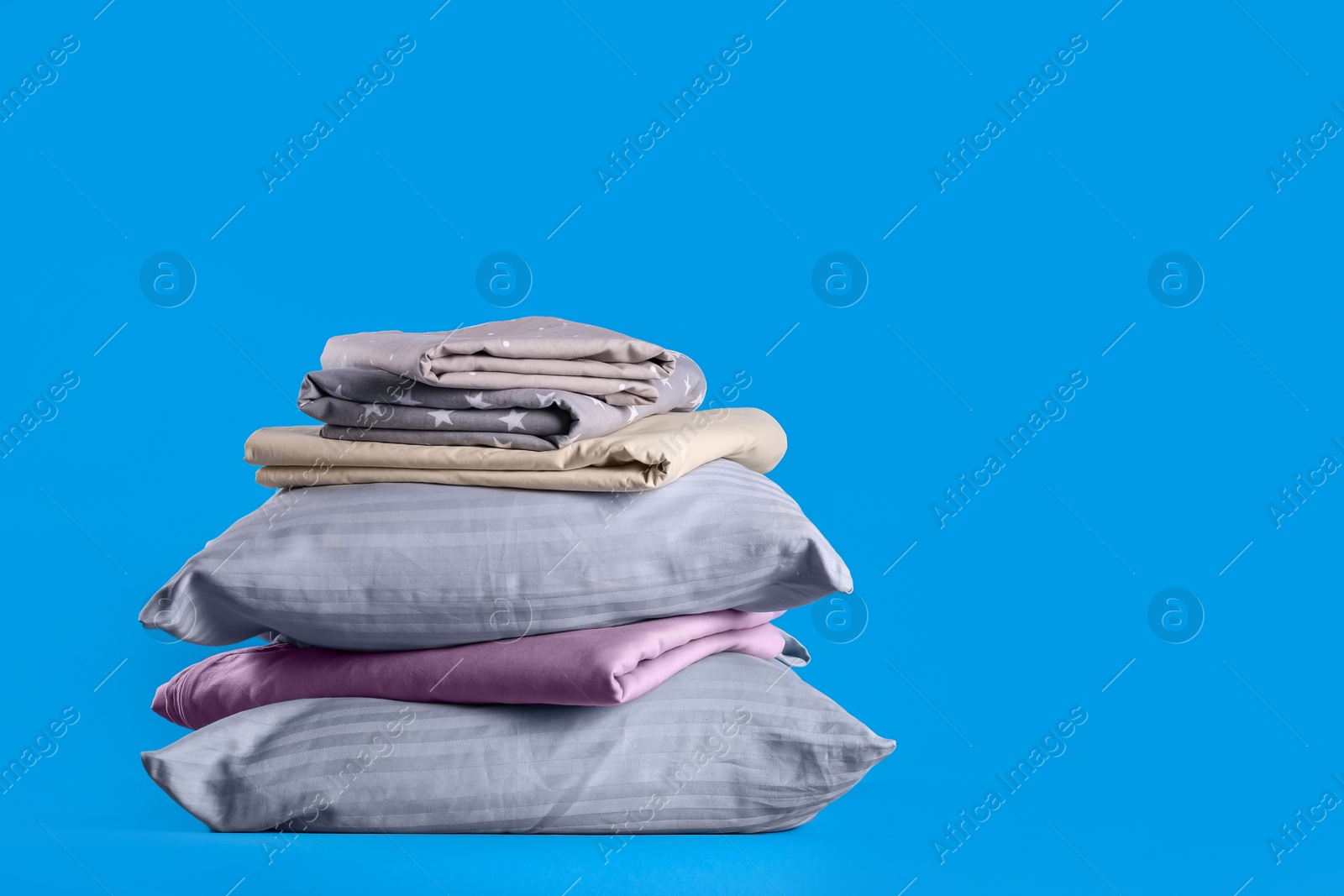 Photo of Stack of clean bed sheets and pillows on blue background. Space for text