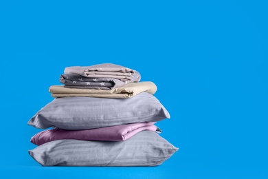 Stack of clean bed sheets and pillows on blue background. Space for text