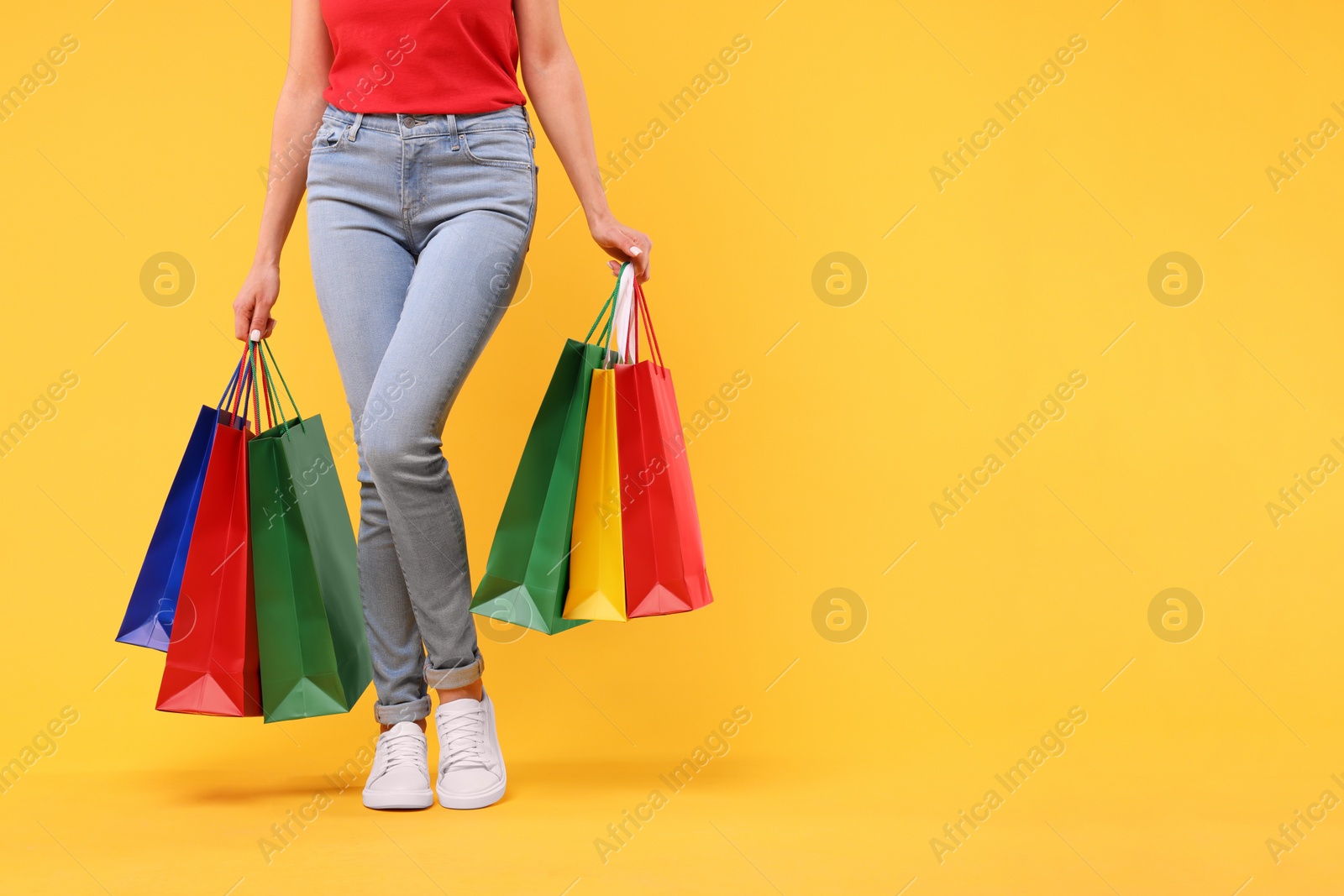 Photo of Woman with shopping bags on yellow background, closeup. Space for text