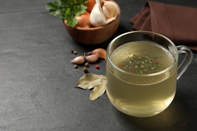Photo of Hot delicious bouillon with dill in glass cup on black table. Space for text