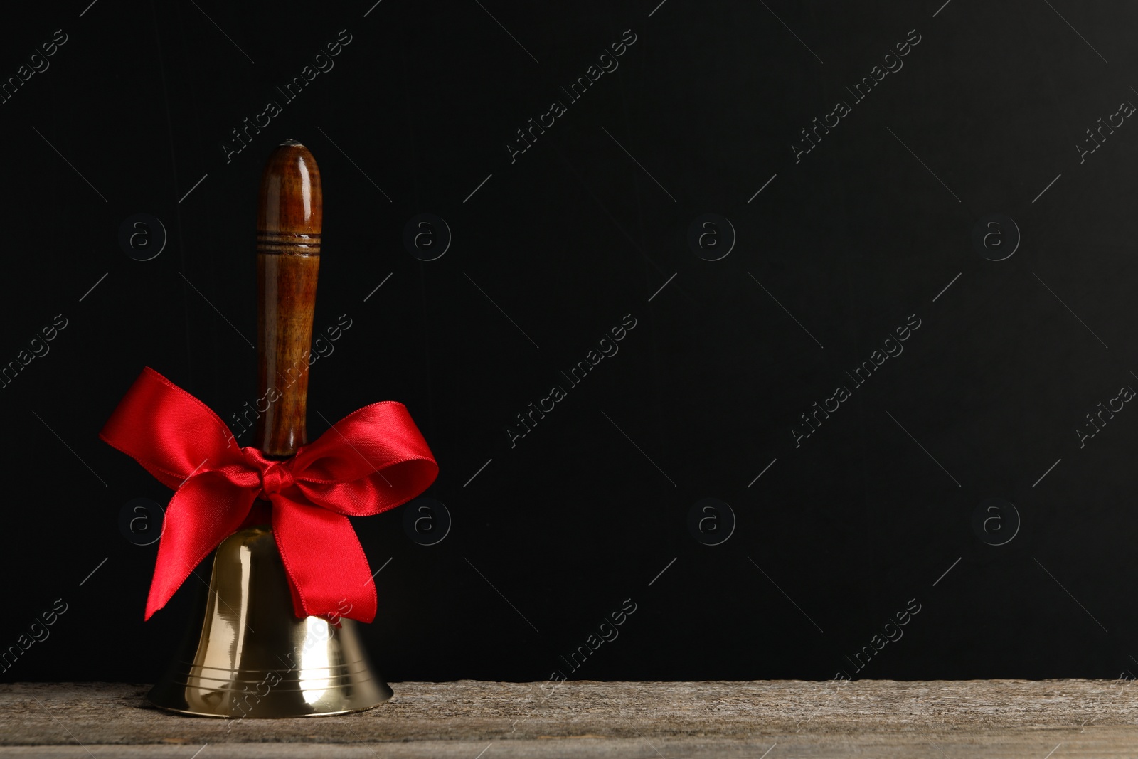 Photo of Golden bell with red bow on wooden table near blackboard, space for text. School days