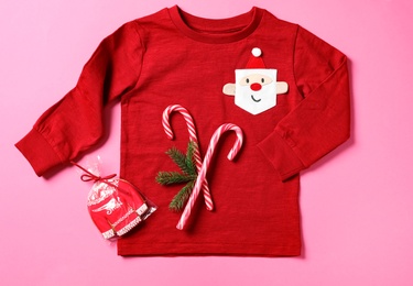 Photo of Red baby jumper, candy canes and gingerbread on pink background, flat lay. Christmas celebration