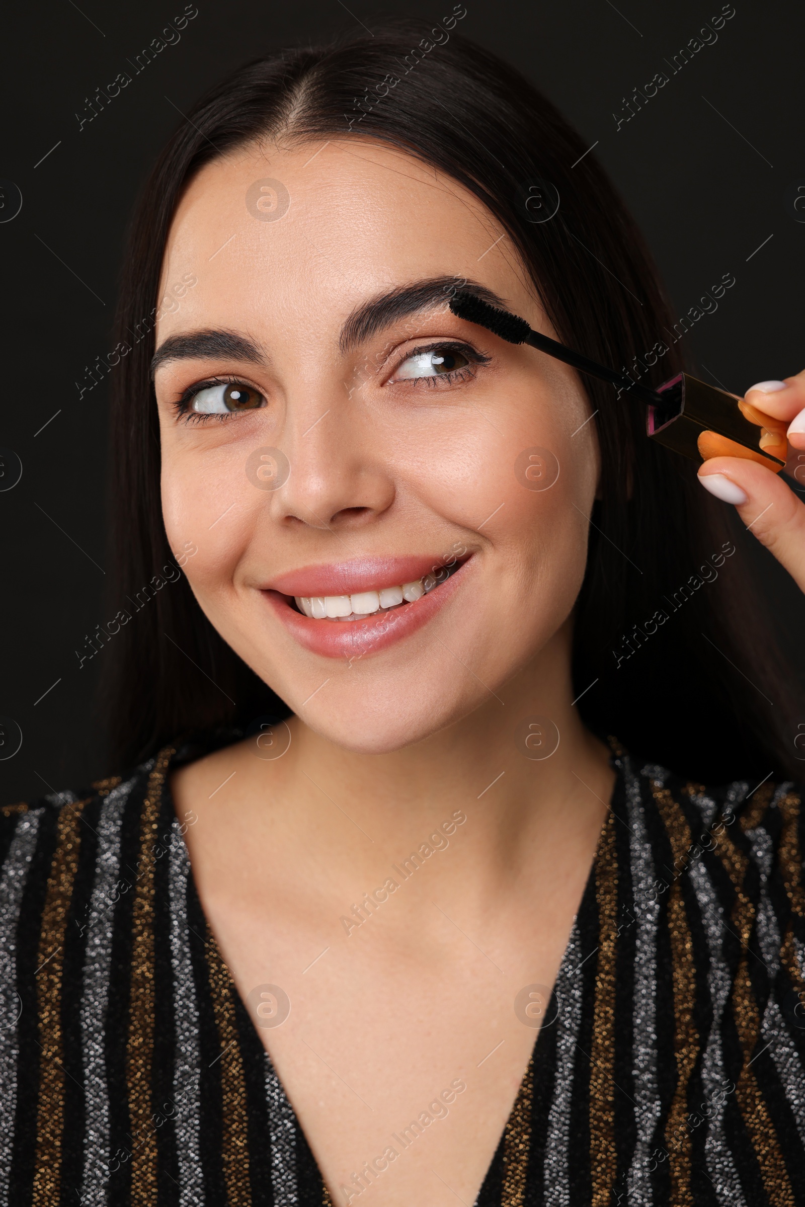 Photo of Beautiful young woman applying mascara on black background, closeup