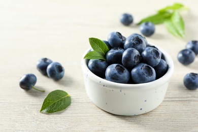 Photo of Bowl of fresh tasty blueberries with leaves on white wooden table, closeup. Space for text