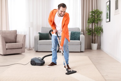 Photo of Young man cleaning carpet with vacuum at home