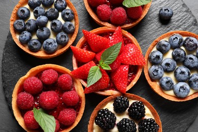 Photo of Tartlets with different fresh berries on slate plate, flat lay. Delicious dessert