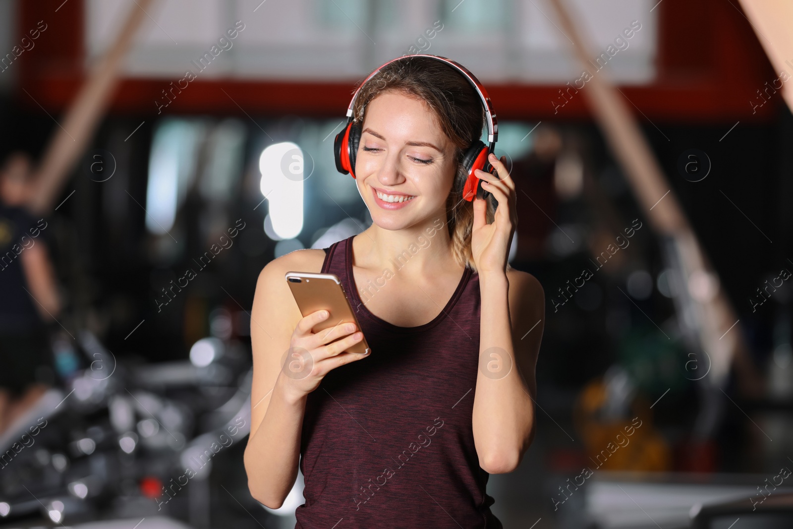 Photo of Young woman with headphones listening to music on mobile device at gym