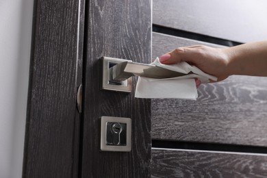 Photo of Woman wiping door handle with paper towel indoors, closeup