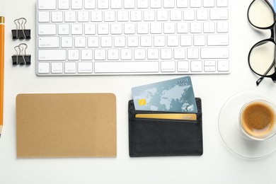 Leather card holder with credit cards, glasses, keyboard, coffee and stationery on white table, flat lay