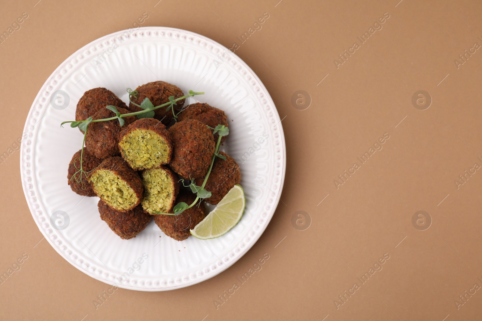 Photo of Delicious falafel balls, lime slice and microgreens on pale brown background, top view. Space for text