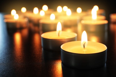 Photo of Wax candles burning on table in darkness, closeup