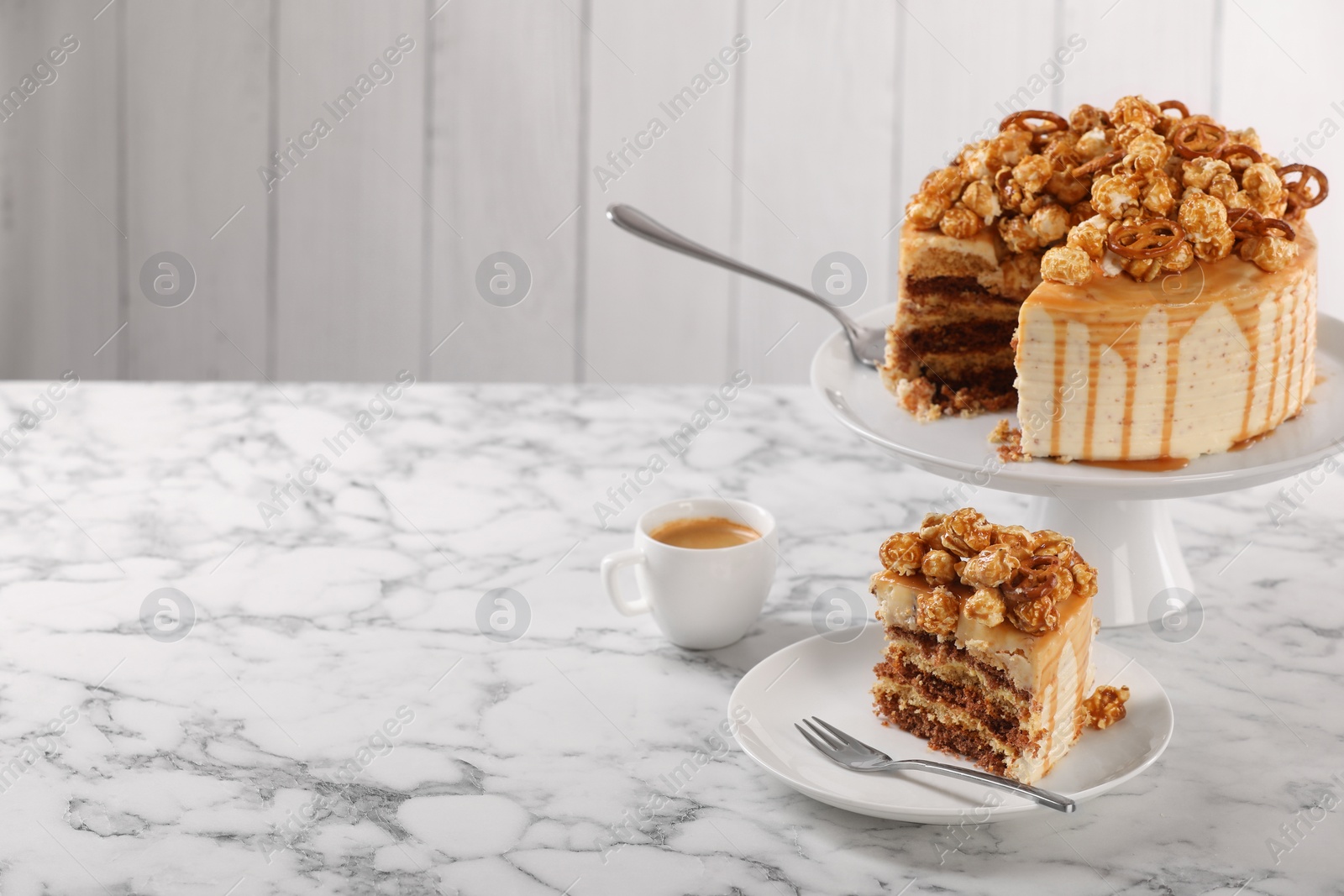Photo of Caramel drip cake decorated with popcorn and pretzels served on white marble table, space for text