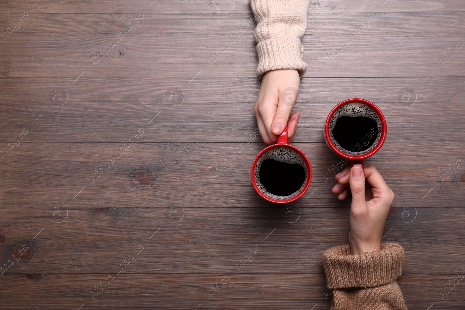 Photo of Women with cups of coffee at wooden table, top view. Space for text