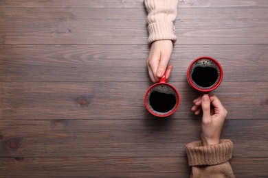 Photo of Women with cups of coffee at wooden table, top view. Space for text