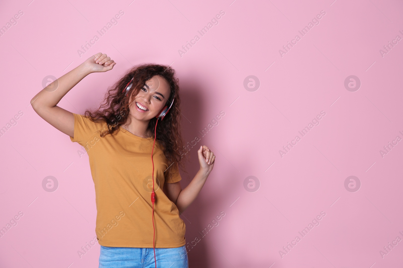 Photo of African-American girl listening to music with headphones on color background, space for text