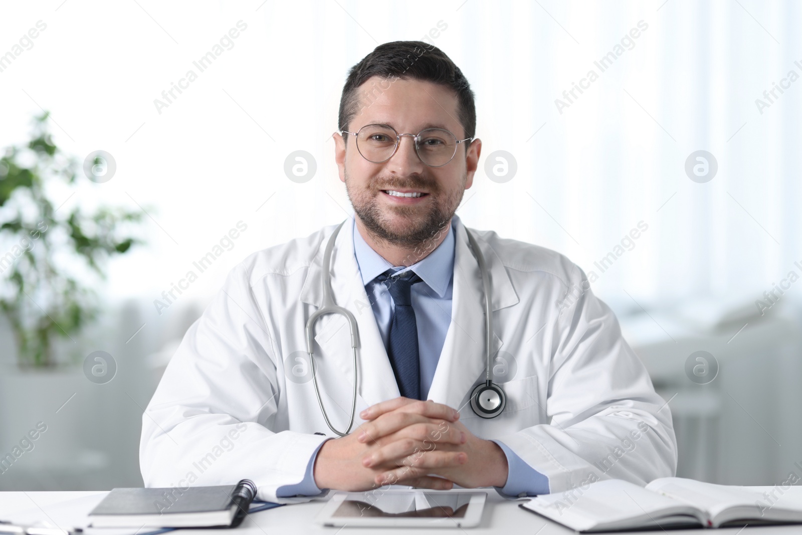 Photo of Smiling doctor with tablet at table in clinic. Online medicine