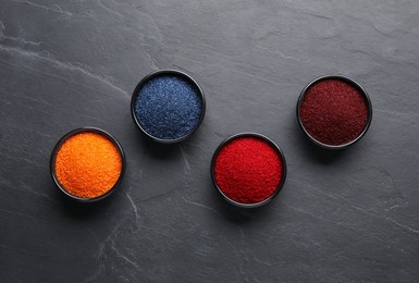 Photo of Bowls of different food coloring on grey table, flat lay