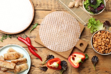 Photo of Rice paper, ingredients and tasty fried spring rolls on wooden table, flat lay