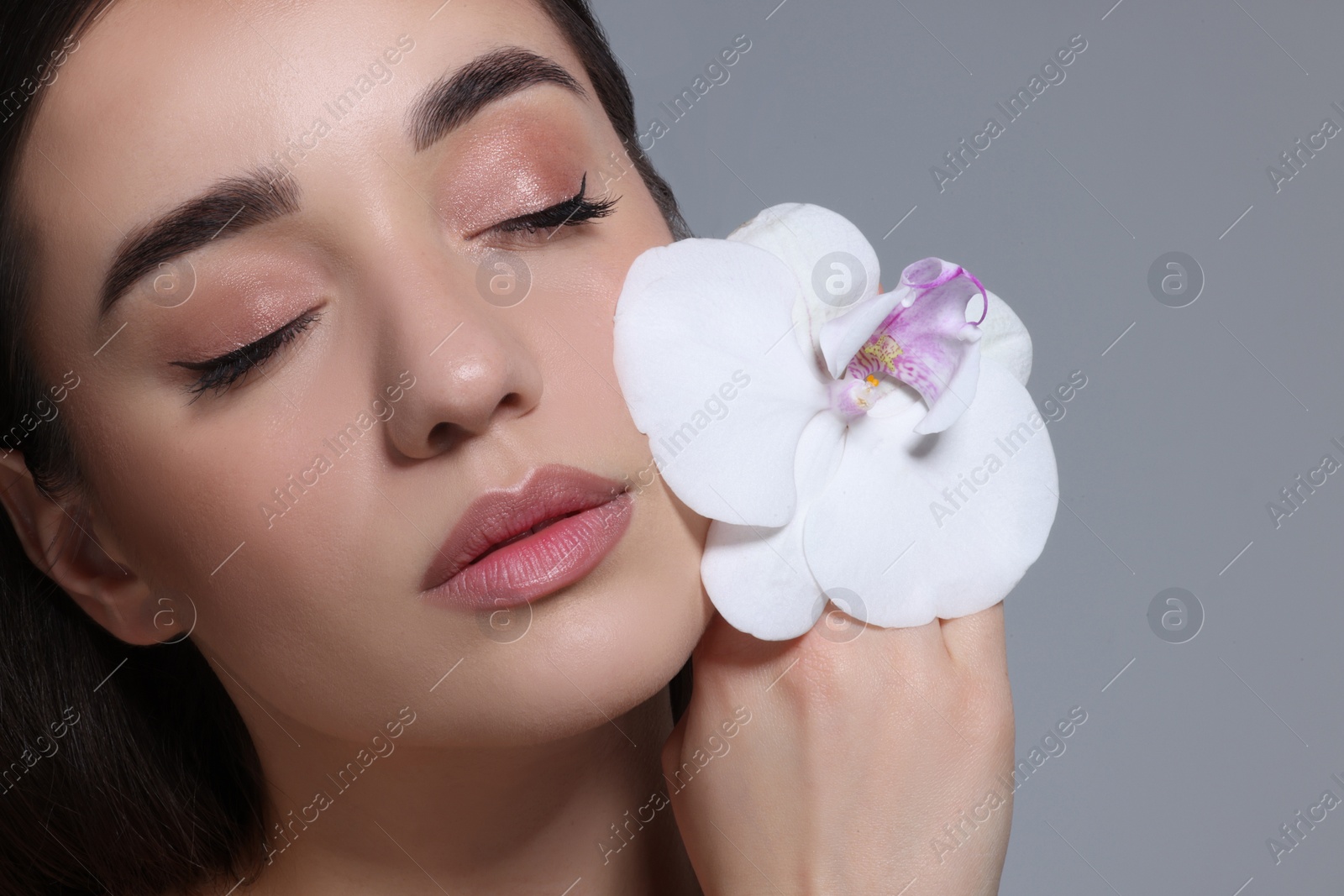 Photo of Portrait of beautiful young woman with orchid flower on grey background