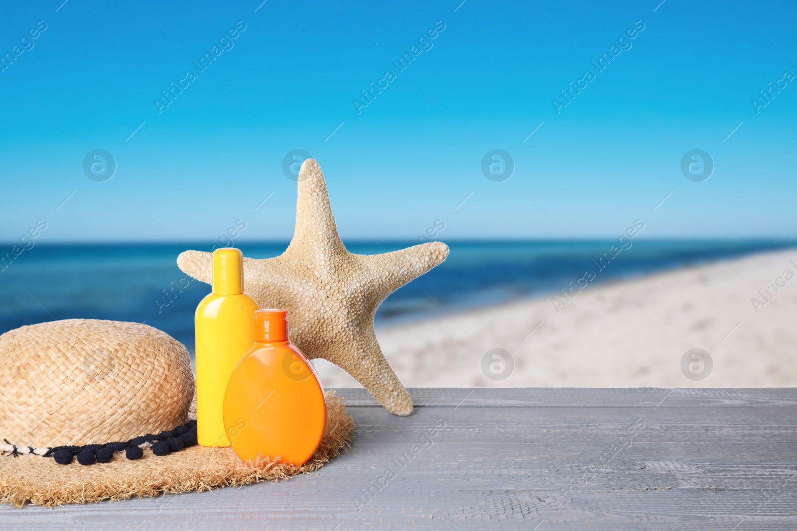 Image of Set of sun protection products and stylish hat on grey wooden table near sea. Space for text